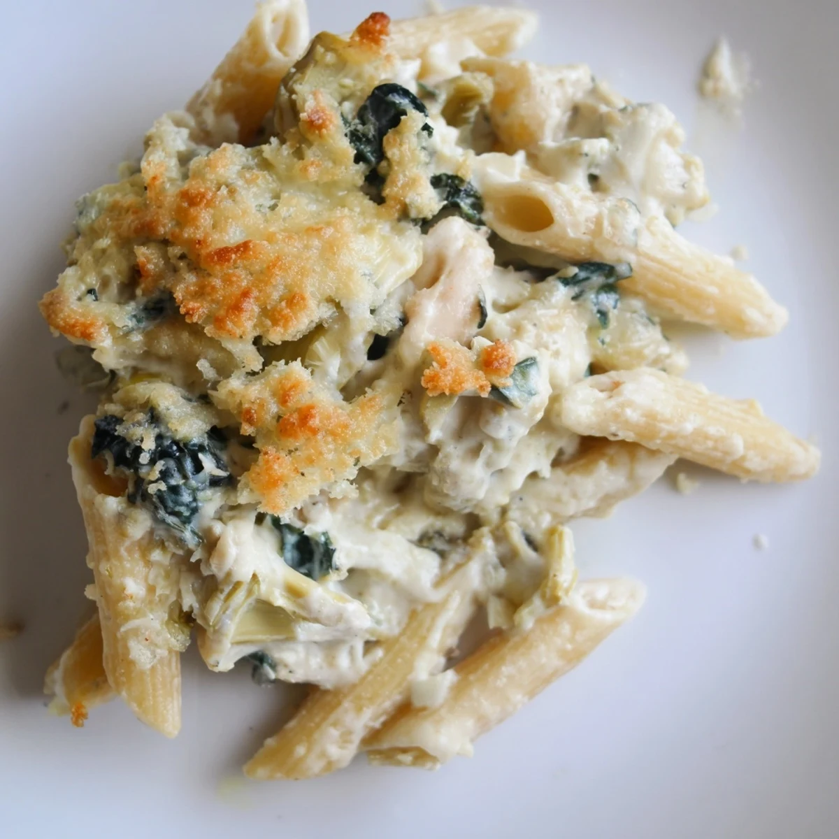 Golden-brown Artichoke Pasta Bake bubbling from the oven, featuring penne with creamy Parmesan sauce, spinach, and marinated artichoke hearts.
