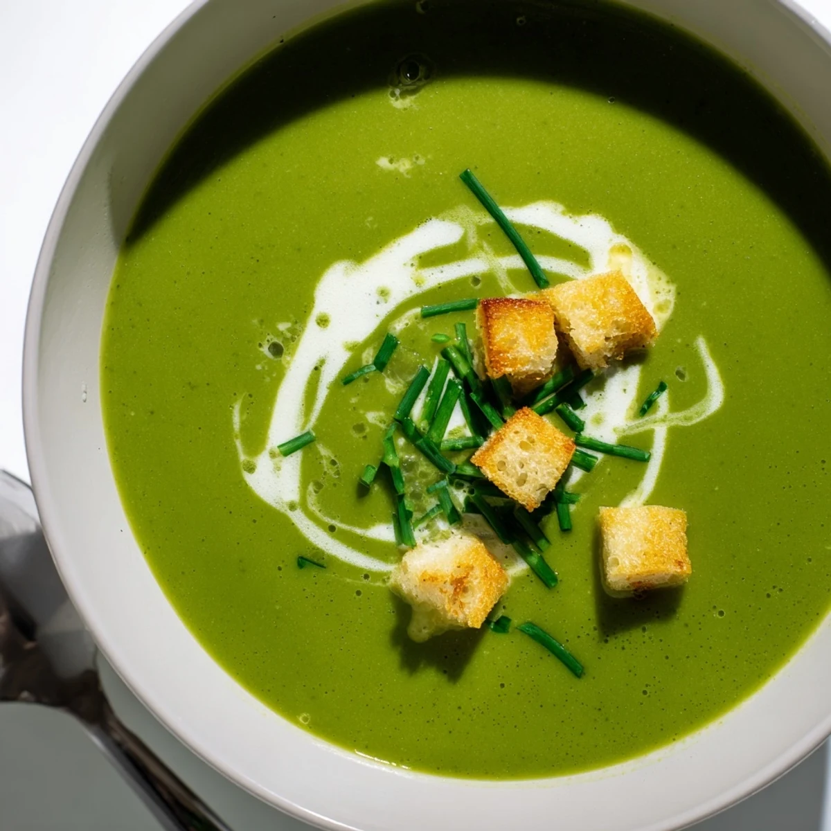 A bowl of homemade Creamy Broccoli Soup garnished with crunchy croutons and fresh chopped chives.
