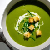 A bowl of homemade Creamy Broccoli Soup garnished with crunchy croutons and fresh chopped chives.