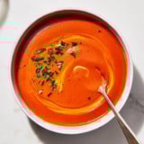 Silky roasted red pepper soup in a white bowl, garnished with a swirl of crème fraîche and fresh parsley.  