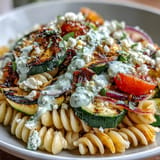 Fresh summer pasta salad featuring charred zucchini, juicy cherry tomatoes, and creamy Cotija cheese, perfect for outdoor gatherings.  