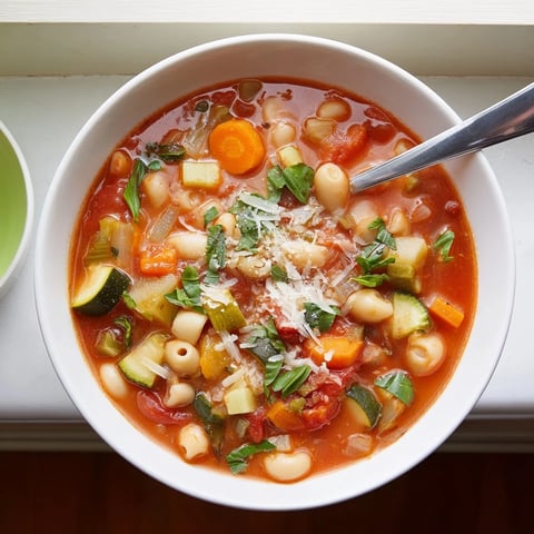 A bowl of steaming Minestrone Vegetable Soup with chunky carrots, celery, and cannellini beans in a rich tomato broth.  