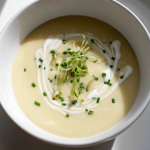 A smooth Celery Root Bisque served in a white bowl, garnished with fresh chives and a drizzle of cream.