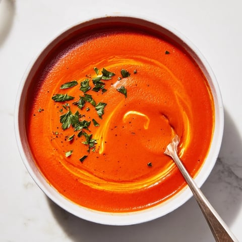 Silky roasted red pepper soup in a white bowl, garnished with a swirl of crème fraîche and fresh parsley.  