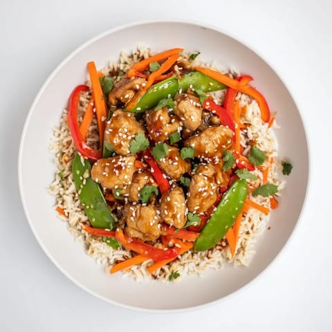 A flavorful Sesame Ginger Rice Bowl showcases tender chicken, colorful vegetables, and a savory sauce.