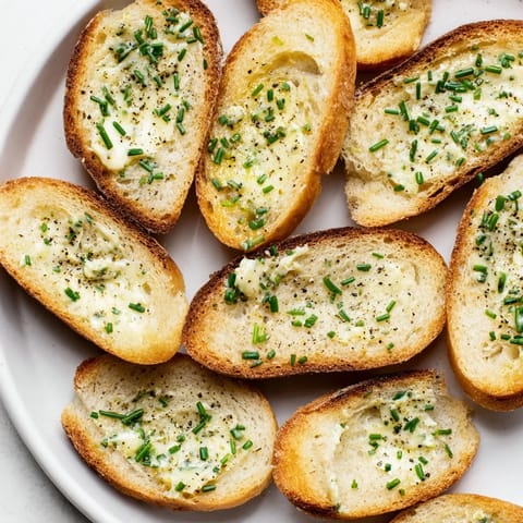 Golden vodka butter crostini slices with a subtle lemon zest and chive garnish on a rustic wooden board.