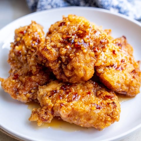 A close-up of fried hot honey butter chicken pieces glistening with glossy sauce, garnished with fresh parsley on a rustic wooden board.