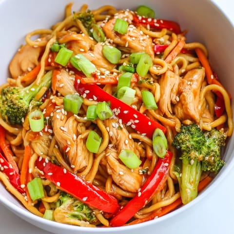 Steaming bowl of Spicy Ramen Stir-Fry topped with toasted sesame seeds and fresh green onions, served alongside chopsticks for an authentic meal.
