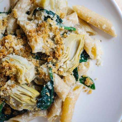 Artichoke Pasta Bake casserole with melted Parmesan, golden breadcrumbs, and tender pasta mixed with spinach and artichokes on a white plate.