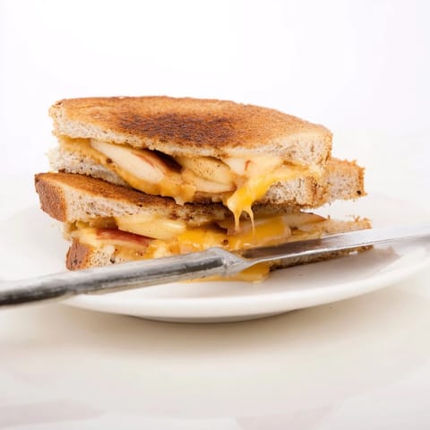 A golden-brown Smoked Gouda & Apple Grilled Cheese sandwich, featuring melted cheese and thin apple slices on toasted sourdough bread.  