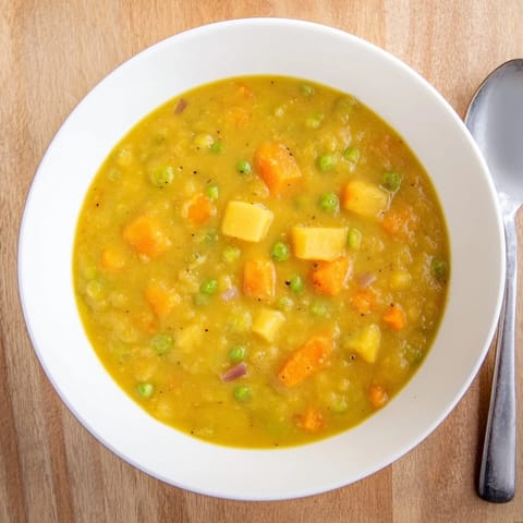 Creamy split pea soup simmering in a pot with carrots, celery, and potatoes.  