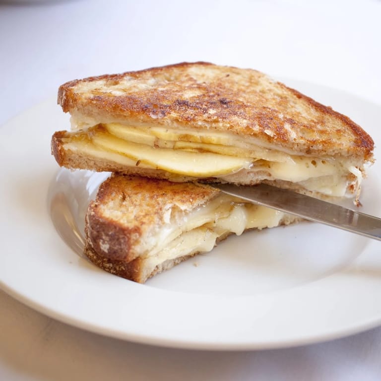 The Smoked Gouda & Apple Grilled Cheese rests on a wooden board, showcasing gooey melted cheese and crisp apple layers.  