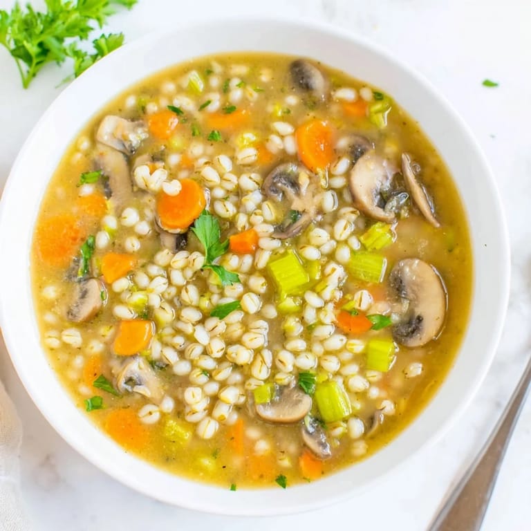 A rustic spoon lifts a ladleful of hearty Mushroom and Barley Soup, garnished with fresh parsley and a slice of crusty bread.